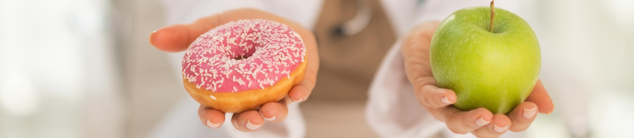Nahaufnahme einer Ärztin, die zwischen Apfel und Donut wählt.