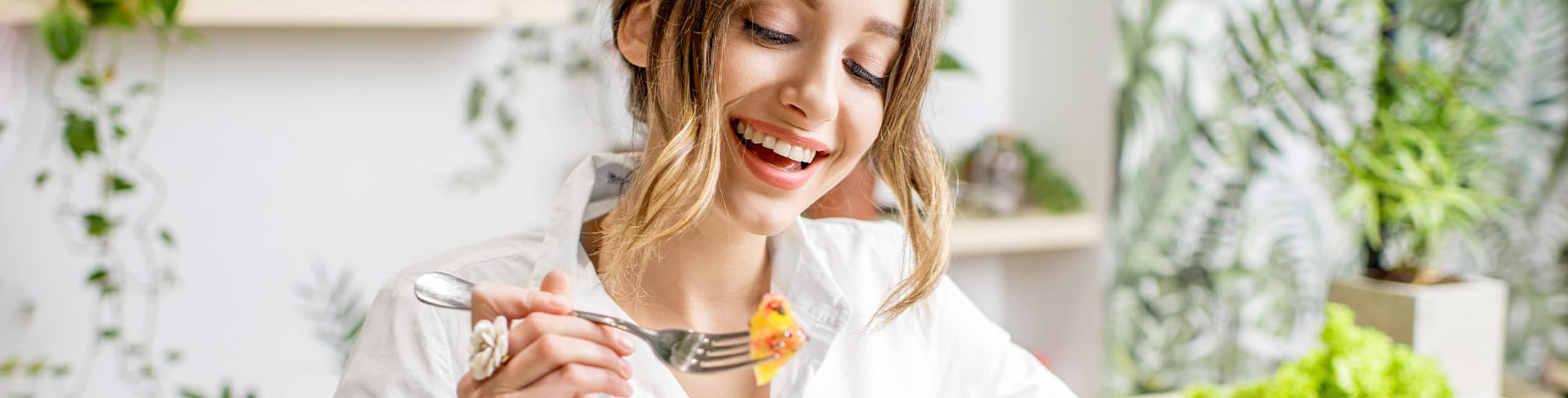 Eine lächelnde Frau isst am Tisch einen gesunden Salat.