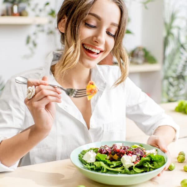 Eine lächelnde Frau isst am Tisch einen gesunden Salat.