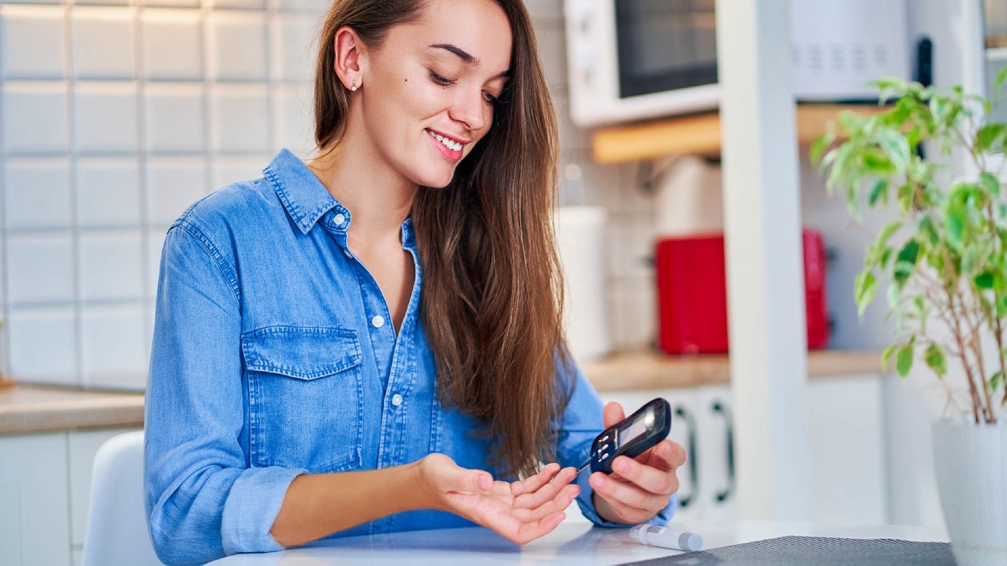 Eine lächelnde Frau misst ihren Blutzucker mit einem Blutzuckermessgerät.