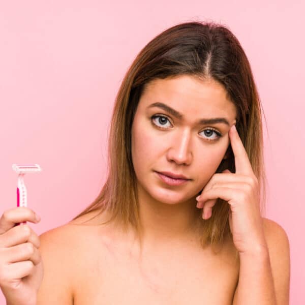 Junge Frau, die ein Rasiermesser in der Hand hält und besorgt aussieht