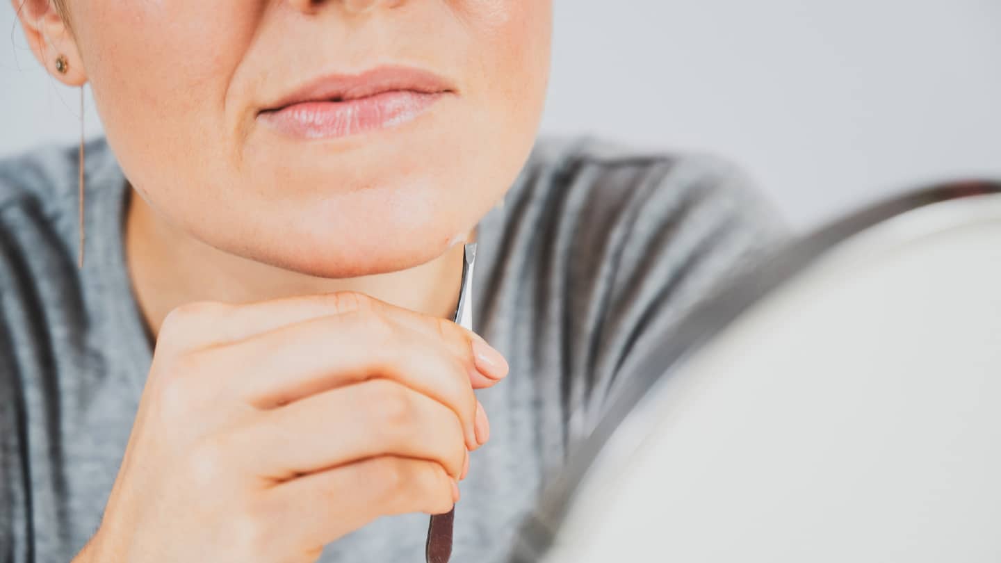 Frau entfernt Haare am Kinn mit einer Pinzette, Nahaufnahme